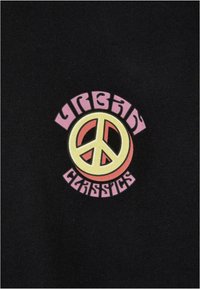 Juodas medvilninis marškinėliai su apvaliu grafiniu piešiniu, kuriame geltoni taikos ženklai, apvadinti oranžine spalva, o aplinkui parašyta "URBAN CLASSICS" rožinės spalvos.