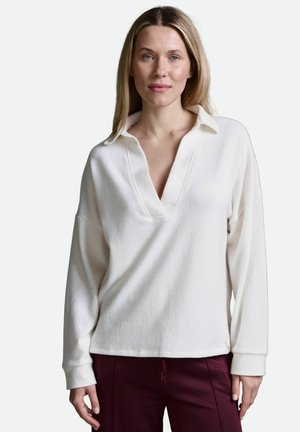 Weißer Pullover mit langen Ärmeln, V-Ausschnitt und Kragen. Weicher Stoff mit entspannter Passform, kombiniert mit kastanienbraunen Hosen. Einfaches Design ohne Muster.