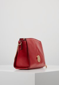 Borsa a tracolla in pelle rossa con una forma strutturata, accessori tonde in oro e una catena per la spalla. Texture liscia, design minimalista.
