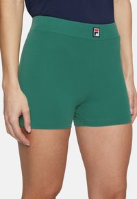 Gröna stretchshorts med en mjuk textur, utrustade med en bred elastisk midjeband och en Fila-logotyp. Designen inkluderar en figurnära silhuett.