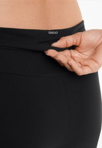 Černé sportovní legíny s hladkým povrchem a vysokým pasem. Logo "OHSAO" je umístěno na horní části zad.