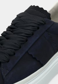 Σκούρο μπλε αθλητικό παπούτσι με επάνω μέρος από σουέντ με υφή, κυματιστές λεπτομέρειες, μαύρα κορδόνια και λευκή σόλα από καουτσούκ. Διαθέτει λεπτομέρειες με ομαλές ραφές.
