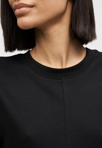 Μαύρο βαμβακερό t-shirt με στρογγυλή λαιμόκοψη και κοντά μανίκια, με ομαλή υφή και διακριτική ραφή κατά μήκος της λαιμόκοψης.