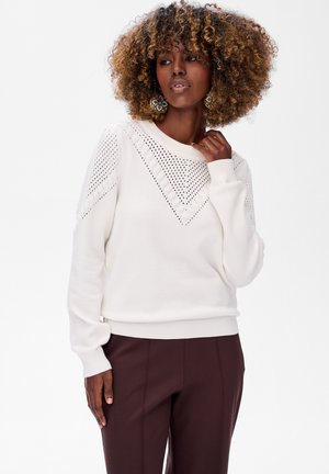 Pull en tricot blanc présentant un design en V avec des détails ajourés le long de l'encolure et des épaules. Bords côtelés aux poignets et à l'ourlet.