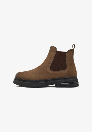 Bruine suede Chelsea boot met elastische zijpanelen, ronde neus, zwarte rubberen zool en een trek lus aan de achterkant voor gemakkelijk aan- en uittrekken.