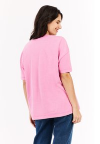 Roze oversized t-shirt met korte mouwen, ronde halslijn en een gladde, zachte textuur. Ontworpen in een losse pasvorm, gecombineerd met donkere jeans.
