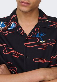 Zwart shirt met korte mouwen, voorzien van rode golvende patronen, blauwe en witte bloemaccenten en een paraplu-design, met een knoopsluiting.