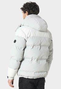 Pehmustettu harmaa talvitakki hupulla, jossa on sileä pinta, joustavat hihansuut ja musta merkki vasemmassa hihaosassa.