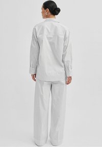 Hvid og grå stribet oversized skjorte og vide bukser sæt, lavet af letvægtsstof med en glat tekstur og knaplukning.