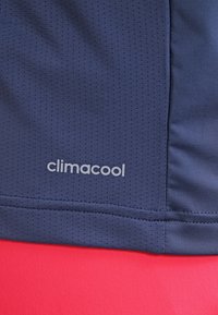 Camiseta atlética de color marino con un patrón texturizado, logo ClimaCool en gris claro, con costura plana y tejido suave sobre un fondo rosado.