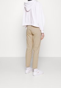 Avskuren vit huvtröja med huva, beige byxor och vita sneakers. Slät tygkvalitet och mer passform med minimal detaljering.