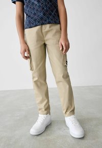 Beige cargobroek met zijzakken, gecombineerd met witte sneakers. Het bovenstuk heeft een marineblauw patroon met geometrische vormen.
