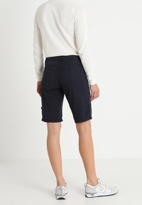 Pantaloni cargo blu navy con una vestibilità rilassata, dotati di tasche laterali e una trama di tessuto liscia, abbinati a scarpe da ginnastica di colore chiaro.