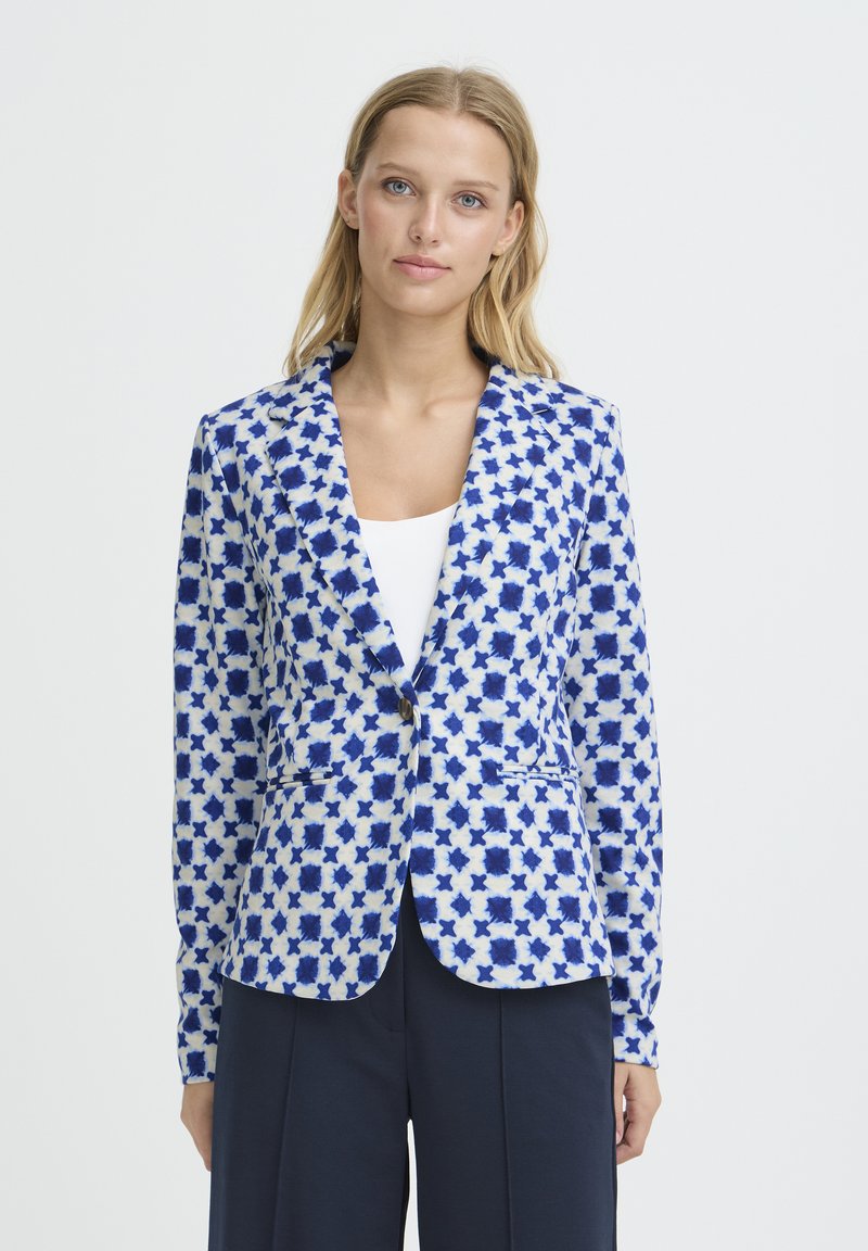 Blazer en tissu blanc avec motifs d'étoiles bleues. Doté d'un col cranté, d'une fermeture à un bouton et de poches avant. Texture lisse.