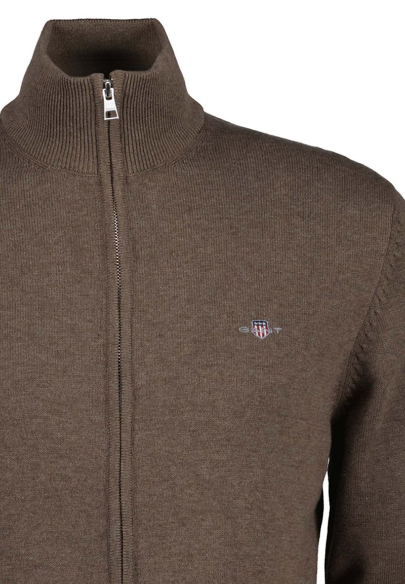 Brown knitted zip-up sweater with ribbed high collar and small embroidered logo on the left chest.