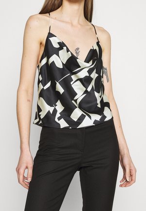 Camisole en satin noir avec motif abstrait blanc, encolure en V, fines bretelles réglables et une coupe drapée. Associée à un pantalon noir ajusté.