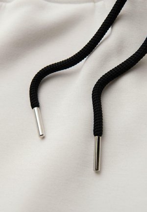 Tela blanca con cordones trenzados negros, con extremos metálicos plateados. El material parece suave y liso.