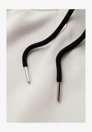 Tela blanca con cordones trenzados negros, con extremos metálicos plateados. El material parece suave y liso.