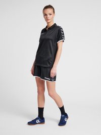 Sort sportsæt med kortærmet polo med krave, mønstrede sideelementer og matchende shorts. Blå løbesko fuldender looket.