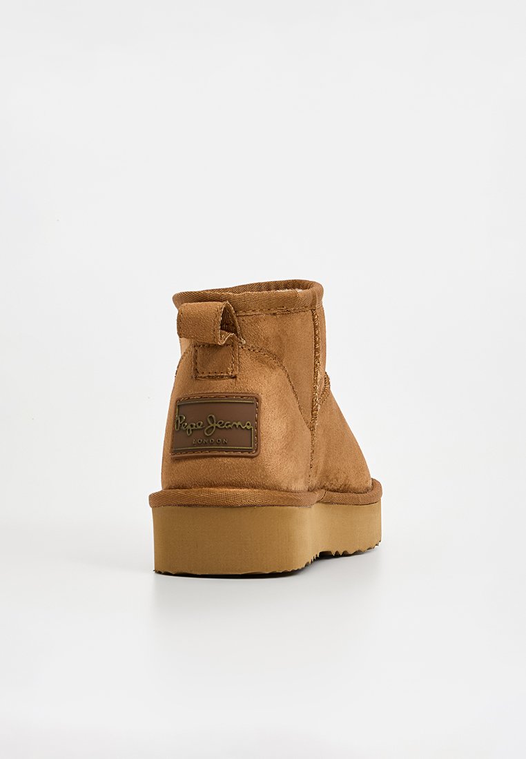 Bruine suède enkellaars met een ronde neus en platte rubberen zool. Beschikt over een logopatch aan de achterkant en een klein aantreklipje voor eenvoudig aan- en uittrekken.