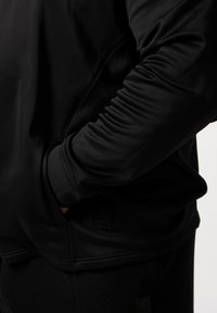 Sort atletisk hoodie med en glat tekstur, der har en afslappet pasform, diskrete sidelommer og en lille mærklabel nær kanten.