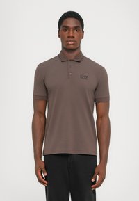 Brun polo skjorte med klassisk krage, med korte ermer og en subtil logo i svart. Glatt tekstur og figurnær design.