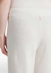 Witte gebreide broek met een zachte textuur en een geribde tailleband, met een klein roze logo label boven de naad aan de achterkant.