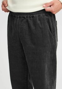 Černé kordové kalhoty mají elastický pas a boční kapsy, s jemně vroubkovanou texturou po celé látce.