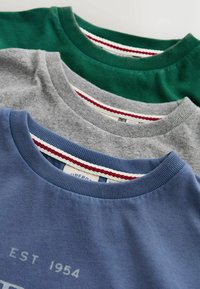 Tři vrstvené mikiny s kulatým výstřihem v modré, šedé a zelené barvě s viditelnými červenobílými proužkovanými štítky na vnitřním límečku.
