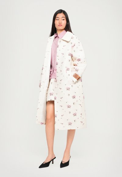 Virágmintás, térdharangú kabát fehér anyagból, rózsaszín virágokkal. Széles gallérral és gombokkal rendelkezik; világos rózsaszín blúzzal és fekete mules-okkal van párosítva.