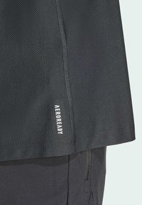 Maglietta sportiva nera con tessuto a rete strutturato. Presenta la scritta "AEROREADY" in bianco vicino all'orlo. Linee pulite e design minimalista.