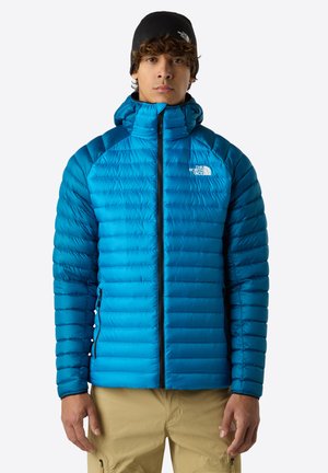 Blue insulated jacket with a zippered front, high collar, and quilted texture. Features logo on the chest and contrasting shoulder panels.