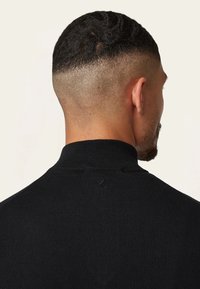 Zwarte coltrui met geribbelde textuur, hoge kraag en een klein geborduurd druppeldetail op de achterkant.