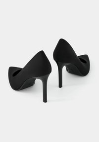 Black high-heeled pumps with a pointed toe, smooth matte texture, and a slender heel. Features a cutout on the side for added design detail.