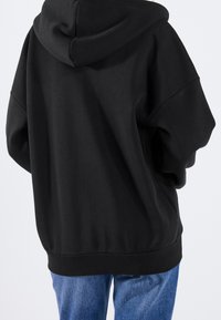 Sweat à capuche noir surdimensionné avec un design spacieux, capuche attachée et poignets côtelés. Assorti à un pantalon en denim bleu.