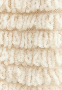 Tessuto in maglia di crema texturizzato con un motivo ondulato, caratterizzato da un filato spesso e morbido che crea un aspetto accogliente.