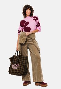 Pull en tricot rose avec un motif floral bourgogne foncé, associé à un pantalon large en velours côtelé marron et un sac fourre-tout à carreaux marron. Chaussures à plateforme marron.
