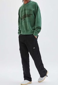 Groene sweatshirt met dierenprint en tekst, zwarte cargo pants met zijzakken en witte sneakers met tankleurige zolen.