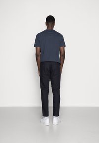 Navy blue short-sleeve t-shirt, slim-fit black pants, and white sneakers, viewed from the back against a plain background.