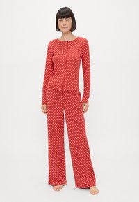 Czerwona piżama w białe kropki składająca się z długiego rękawa koszuli zapinanej na guziki oraz spodni z szerokimi nogawkami. Miękka tkanina z białymi okrągłymi wzorami.