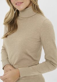 Beżowy sweter z golfem, wykonany z miękkiego materiału dzianinowego, z dopasowanymi, długimi rękawami i ściągaczami. Prosty, bezszwowy design z minimalnymi detalami.