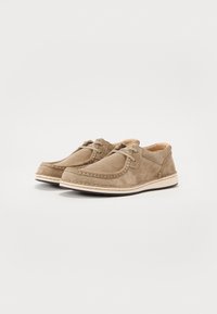 Scarpe in suede beige con punta tonda e cuciture a contrasto, con design allacciato e suola bianca flessibile.