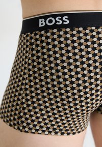 Schwarze Boxershorts mit einem geometrischen Muster aus Sechsecken in Beige und Creme. Der Bund zeigt das "BOSS"-Logo in Weiß.
