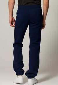 Marinblå mjukisbyxor av mjukt tyg, med avsmalnande passform och elastiska muddarna vid anklarna, designade för komfort och rörelsefrihet.