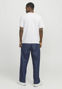 White short-sleeved t-shirt paired with dark blue baggy jeans. Visible back seams and two pockets on the jeans. Footwear is white sneakers.