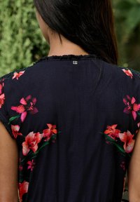 Ziedu tops tumši zila auduma krāsā ar spilgti rozā un oranžiem ziedu rakstiem uz pleciem. Mīksta tekstūra un nodiluša mala detaļa.