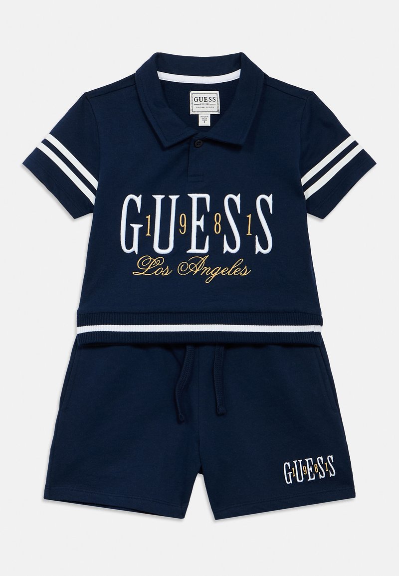 Σετ δύο τεμαχίων σε ναυτικό μπλε, που αποτελείται από κοντομάνικο πόλο με λευκές ρίγες και κεντημένο λογότυπο "GUESS"· ταιριαστό σορτς με κορδόνι και λεπτομέρεια λογοτύπου.