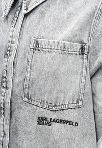 Szara koszula dżinsowa z wyprofilowanym kołnierzykiem, zapięciem na guziki oraz kieszenią na piersi z czarnym wyszytym logo "KARL LAGERFELD JEANS."
