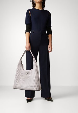 Borsa a tracolla perforata grigio chiaro con un design morbido, caratterizzata da un manico liscio e un discreto logo, su uno sfondo tenue.
