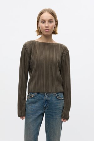 Haut marron plissé à manches longues avec un large col, associé à un jean bleu déchiré. Le tissu texturé et les détails à coupe ajustée sont marquants.